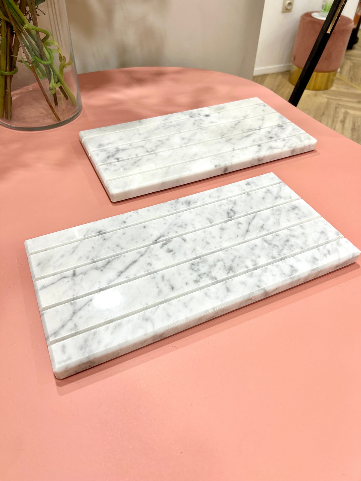 Two grooved white Marble Tray DISPLAY slabs on a pink table, one with card slots in front and a vase of greenery behind.