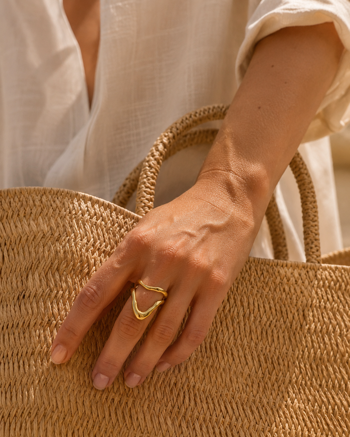 Model rests her hand on a woven straw bag wearing the gold Mare & Soleil RING's pointed V-shaped loop.