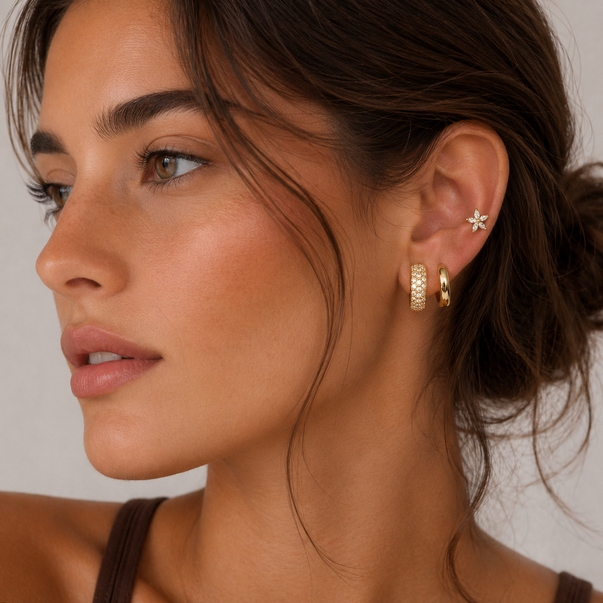 Close-up of a model wearing the three-piece Marigold SET gold earrings in clear stones stacked along her ear.