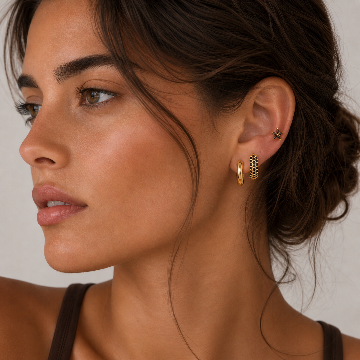 A model wears the three-piece Marigold SET gold earrings in black stacked along her ear, including a pave hoop.