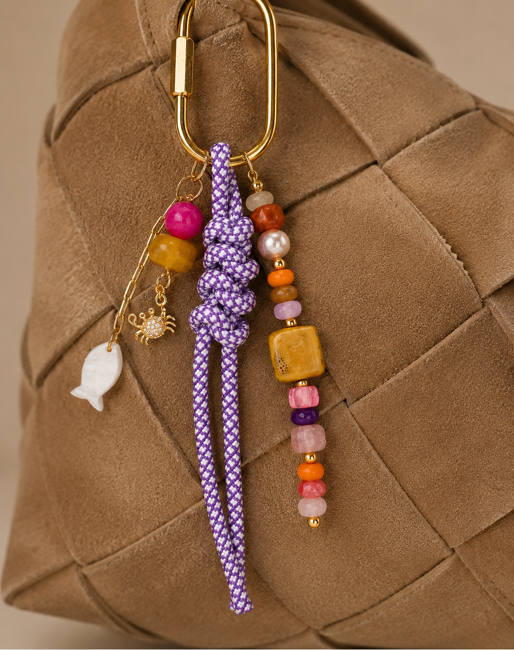 Folie à Trois Marisol BAG CHARM in purple rope with colorful beaded strands and gold fish and crab charms, clipped to a woven tan bag.