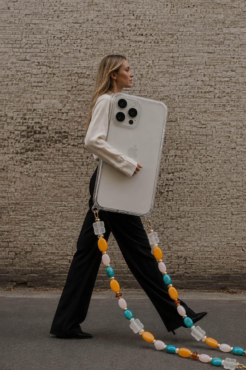 Woman walks past a concrete wall carrying an oversized phone case on a turquoise and mustard beaded chain — Folie à Trois Marisol phone chain