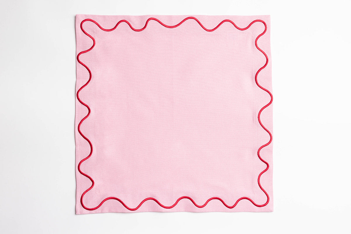 Single pink Maude napkin with a red wave-trim border, laid flat and square on a white background.