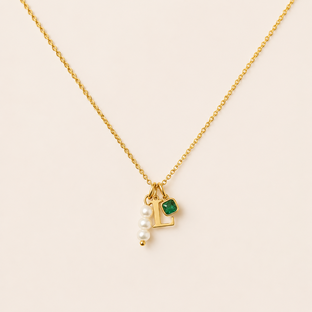 The Minimal NECKLACE in close-up, a gold L initial charm, cluster of pearl beads, and a square emerald charm on a fine chain.