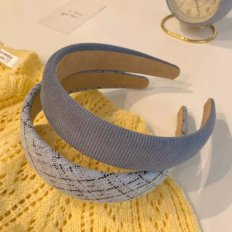 Two padded headbands, one ribbed blue grey and one grey herringbone tweed, resting together on a yellow knit sweater.