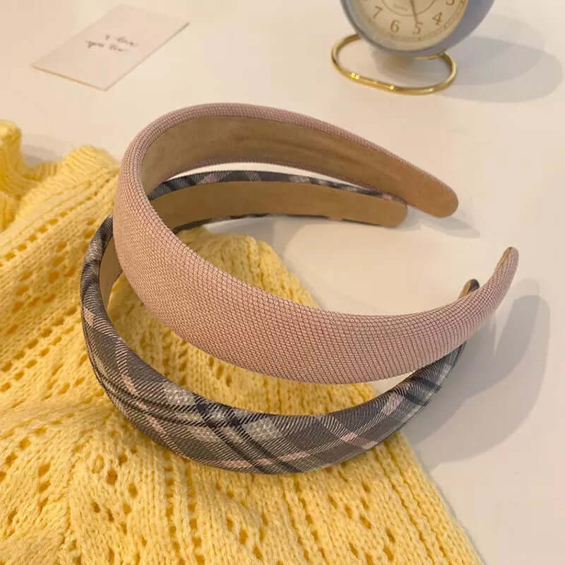 Two padded headbands, one dusty pink ribbed and one grey plaid, resting together on a yellow knit sweater.