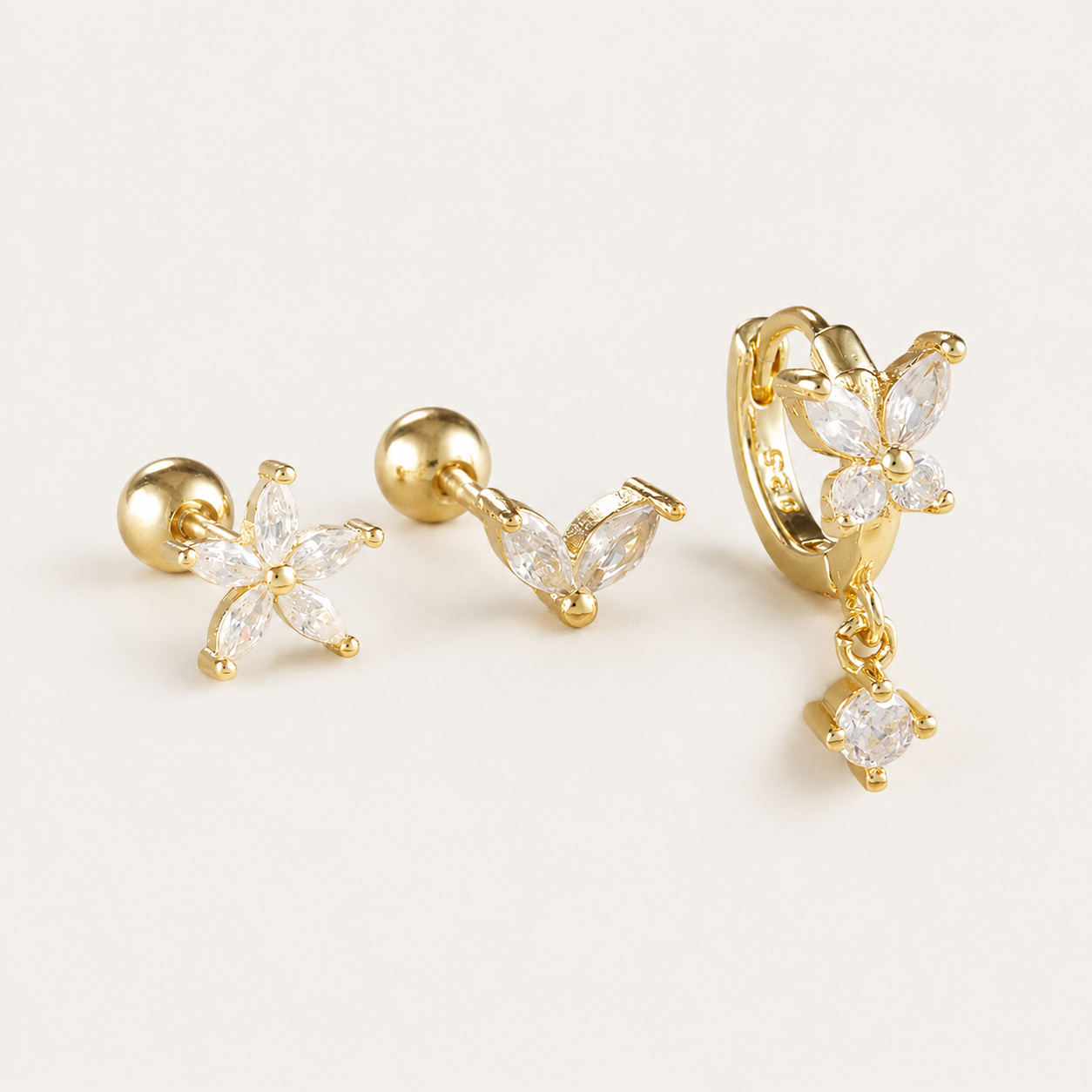 Three-piece Misha SET gold earrings in clear stones: a flower stud, a small V-shaped stud, and a flower hoop with a drop charm.