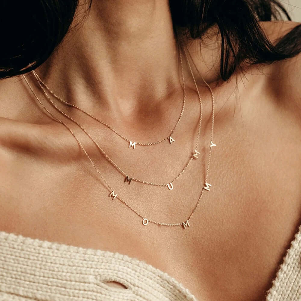 The Mommy NECKLACE layered with MAMA and MUM necklaces at the neckline, three fine gold chains with dangling letters.