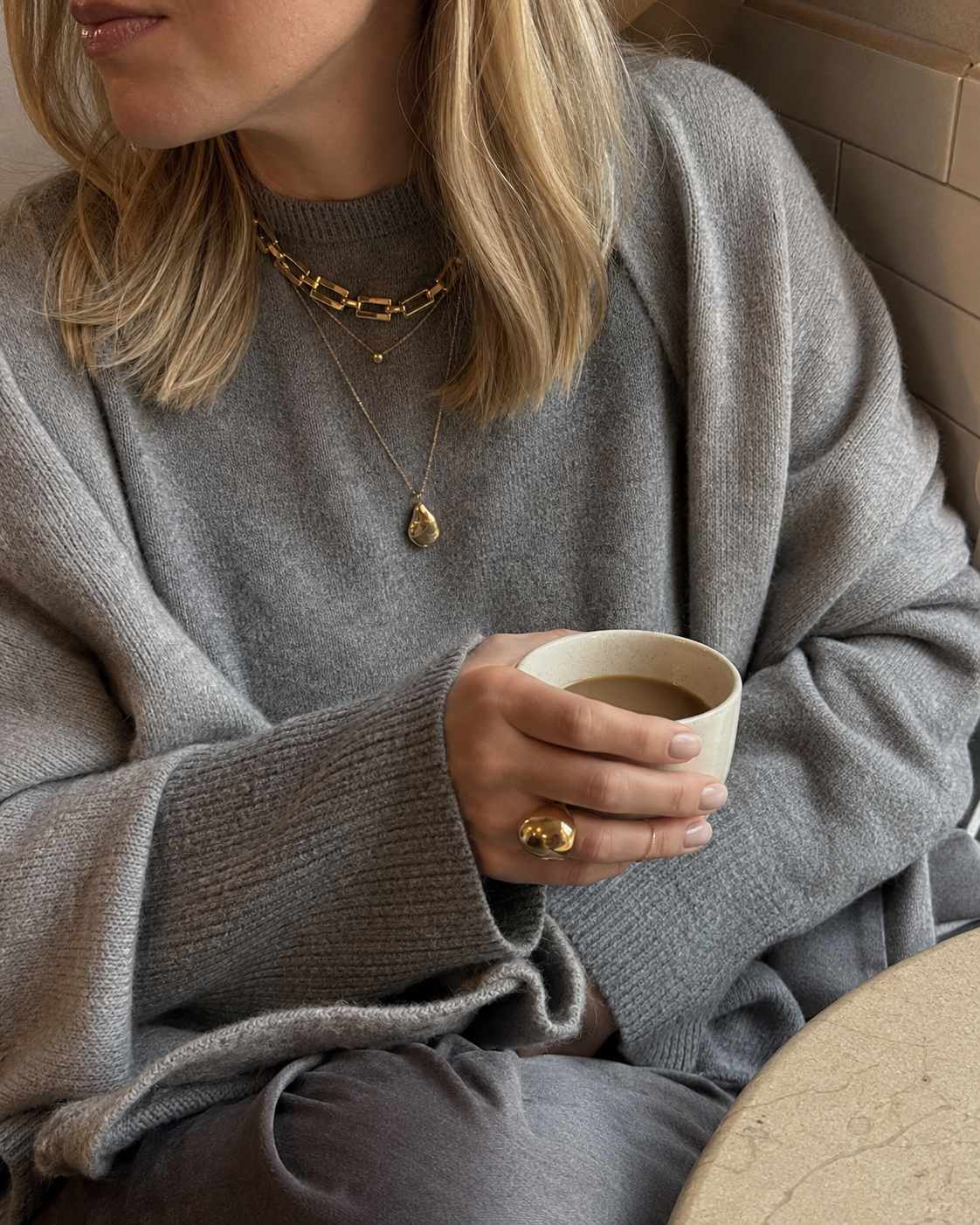 Model wears the gold Folie à Trois Mona NECKLACE, a flat panther-link chain layered with another necklace over a knit sweater.