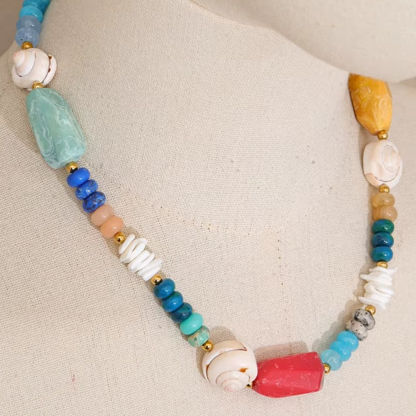 The Mykonos NECKLACE displayed on a mannequin bust, its mix of gemstone, shell, and coral beads shown in close detail.