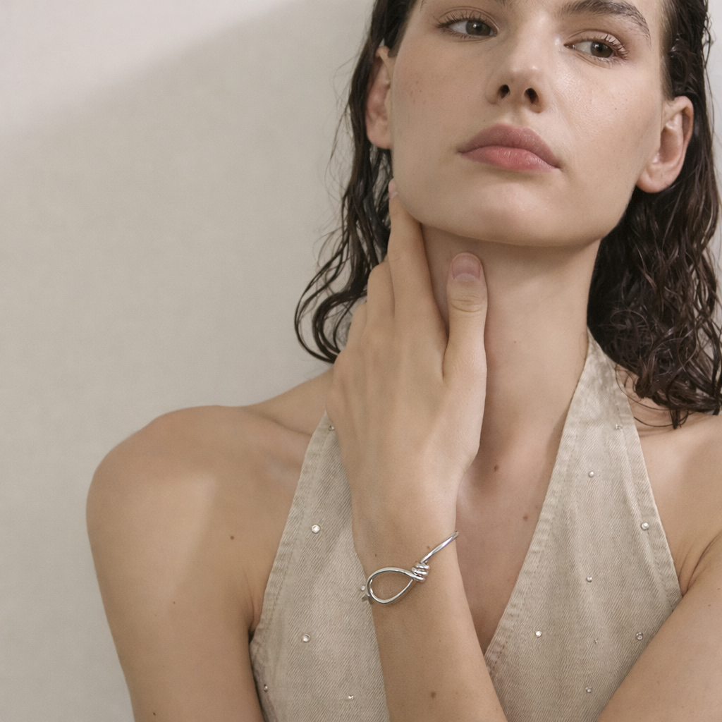 Neeve BRACELET worn in silver on the wrist, model touching her neck in a beige halter top.