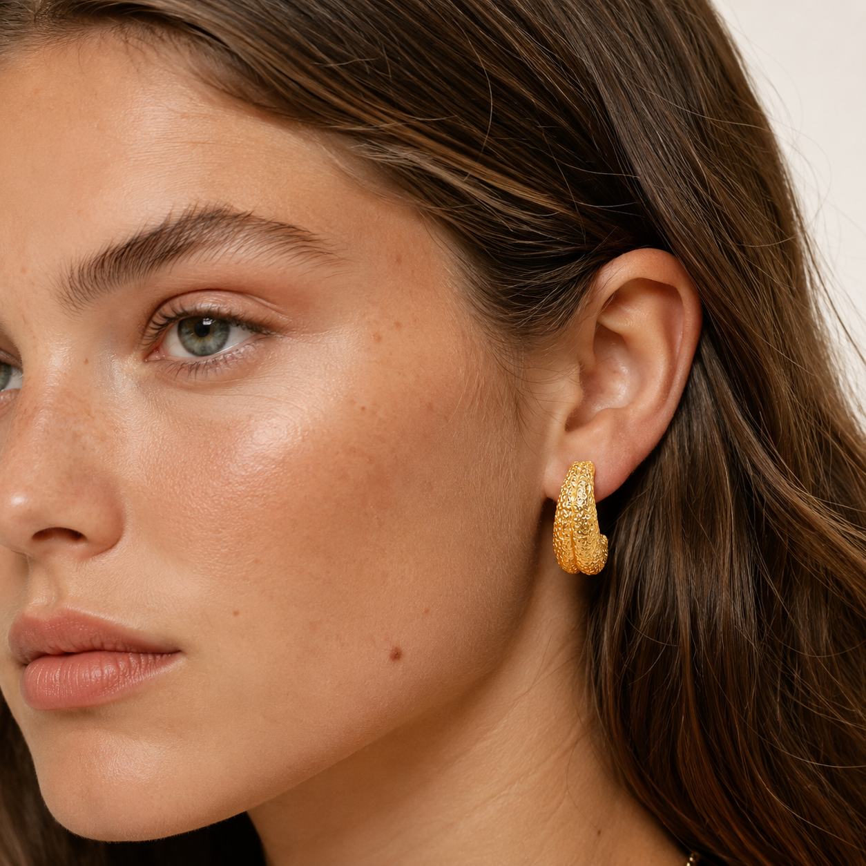Model wears the Folie à Trois Nerja EARRINGS, a gold hoop earring with a textured, bark-like hammered surface.