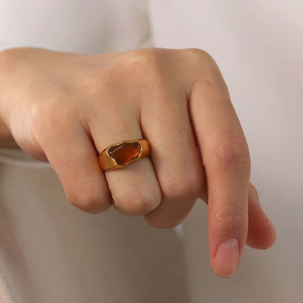 Close-up of a fist wearing the gold signet-style New Fashion RING set with an amber cabochon stone.
