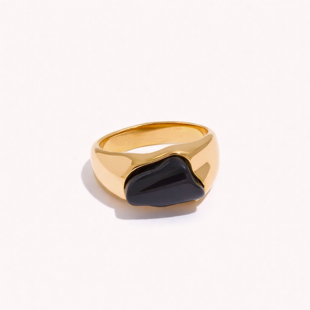 Gold signet-style New Fashion RING set with an irregular black cabochon stone, shown at an angle on a cream backdrop.
