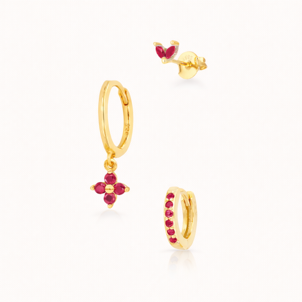 The New Perspective SET in gold with ruby red stones, featuring the marquise stud, flower dangle hoop, and pavé hoop in a studio shot.