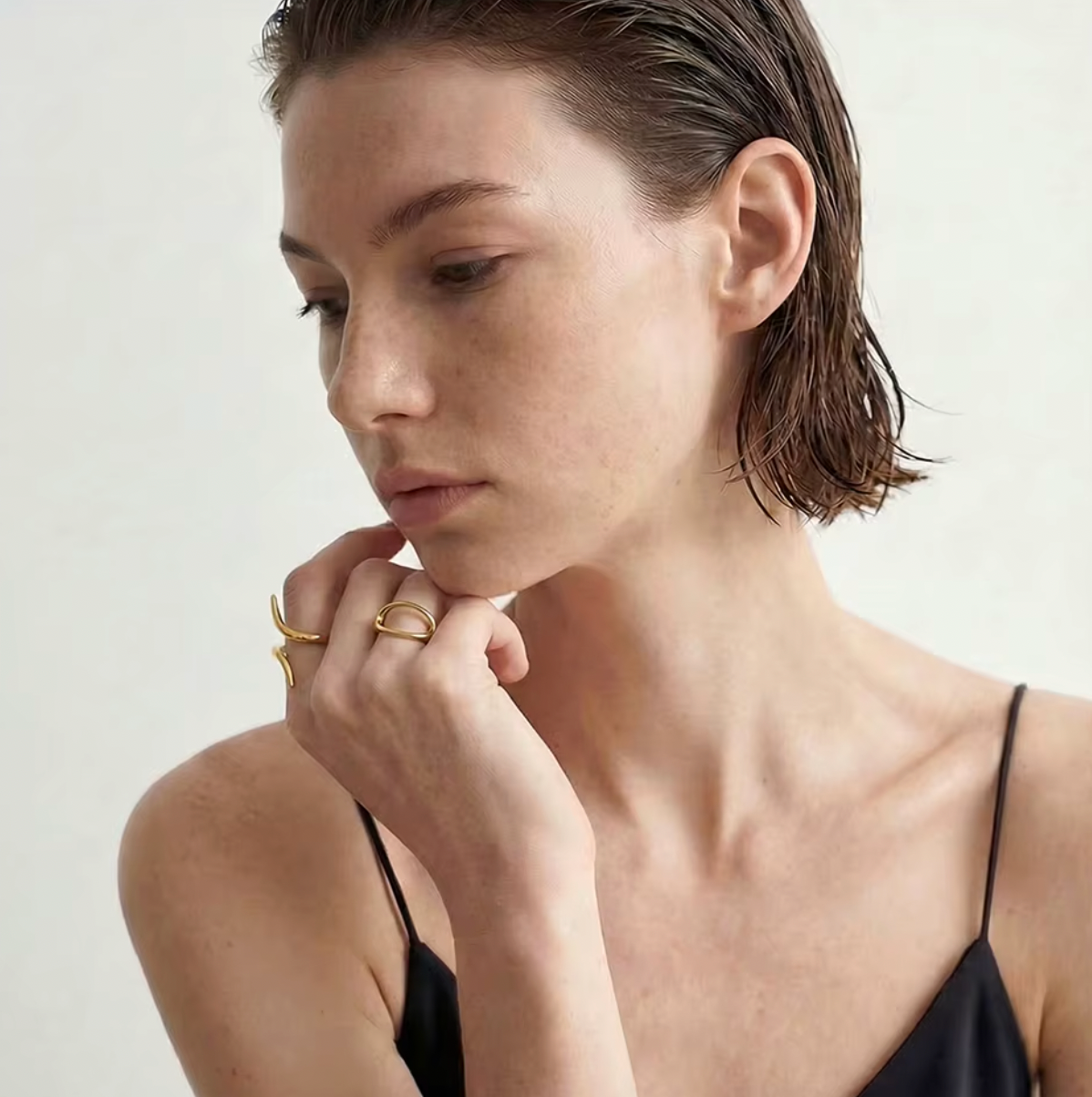 Model rests her chin on a hand stacked with the gold Obsidian RING and an open oval ring.