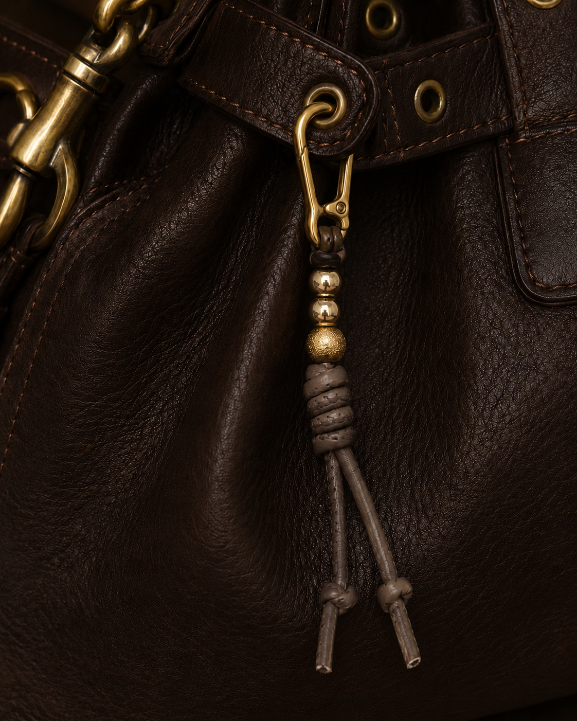 Folie à Trois Oliva BAG CHARM, a taupe leather tassel with gold and wood beads, clipped to dark brown bag hardware.