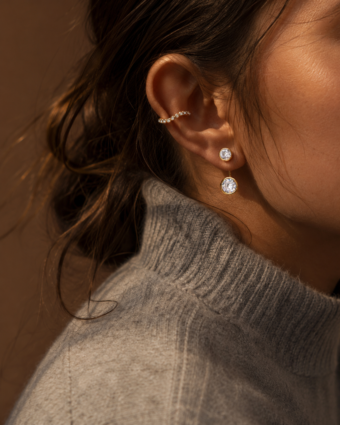 Model wears the gold Folie à Trois Ondine EARRINGS, a two-stone zirconia ear jacket, styled with an ear cuff and grey turtleneck.