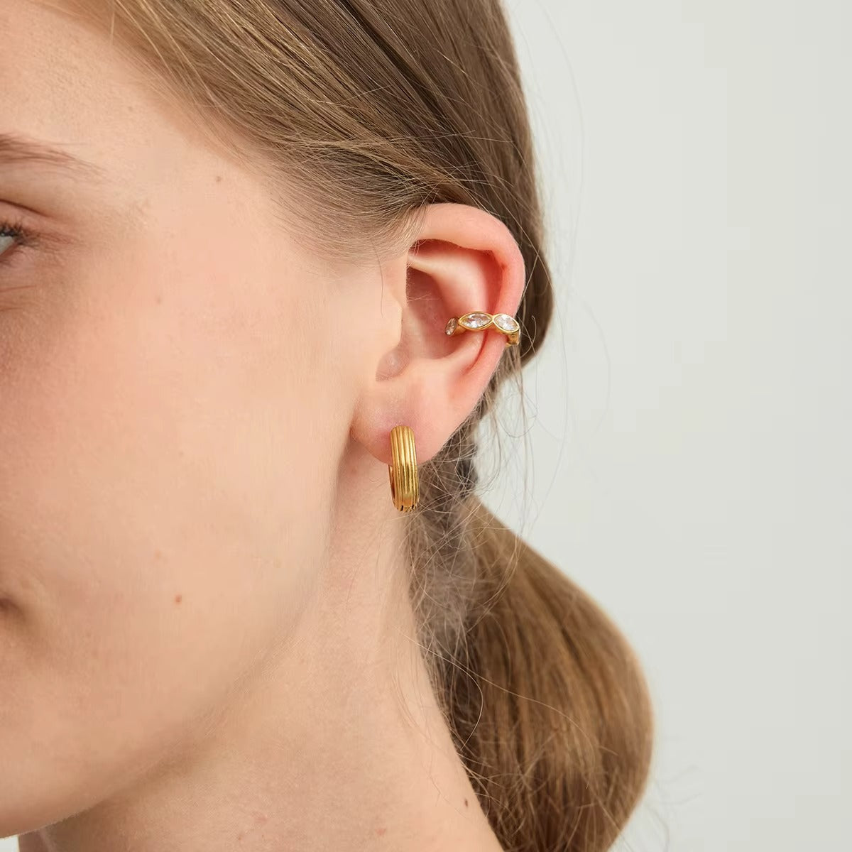 Close-up of the Overdrive ear cuff worn on the upper ear, showing the marquise crystals above a ribbed gold hoop.