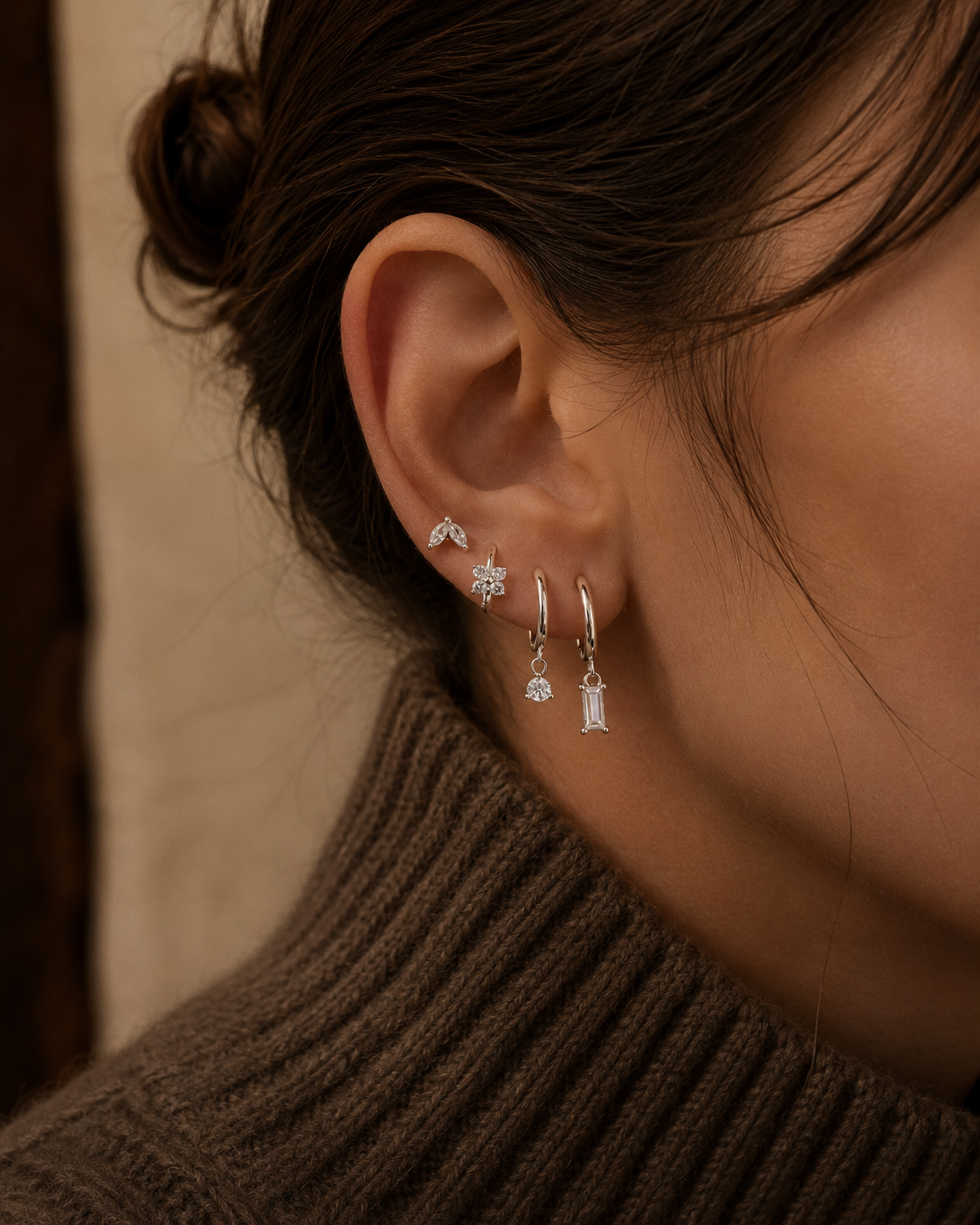Model wears the Folie à Trois Perfect Earparty SET in clear crystal stacked along the ear, layering studs with a baguette and round crystal drop hoop.