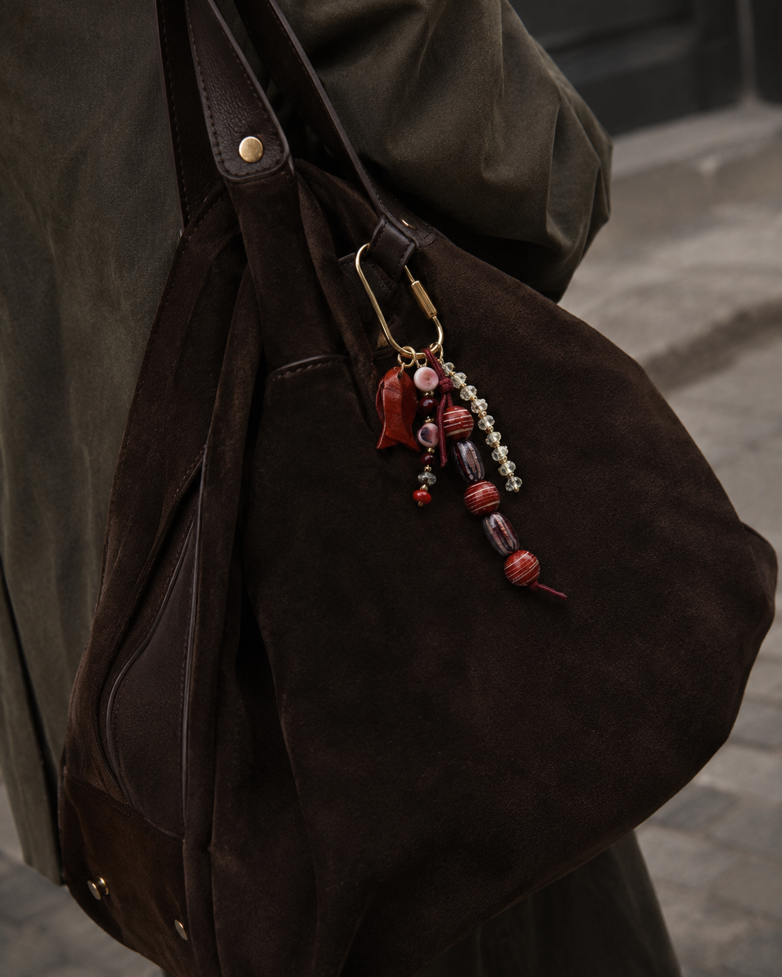Folie à Trois Pescado BAG CHARM in burgundy and purple beaded strands with a leaf-shaped enamel charm, clipped to a dark suede bag.