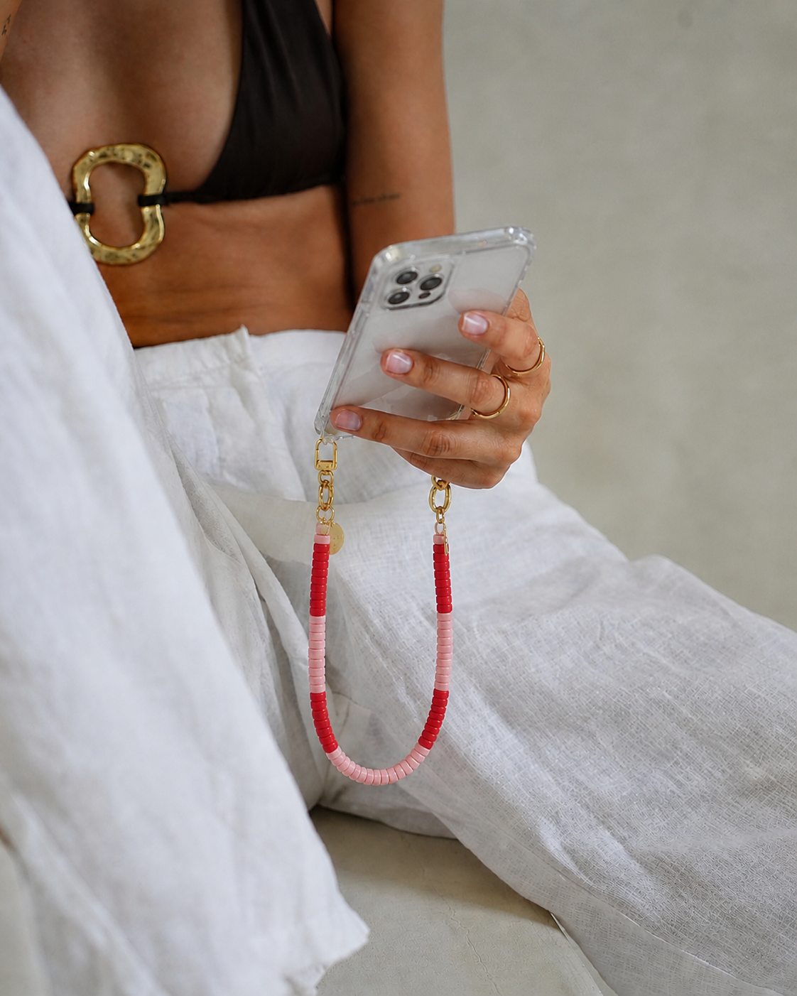 Woman holding a phone case attached to a red and pink heishi bead Poppy SHORT PHONE CORD.