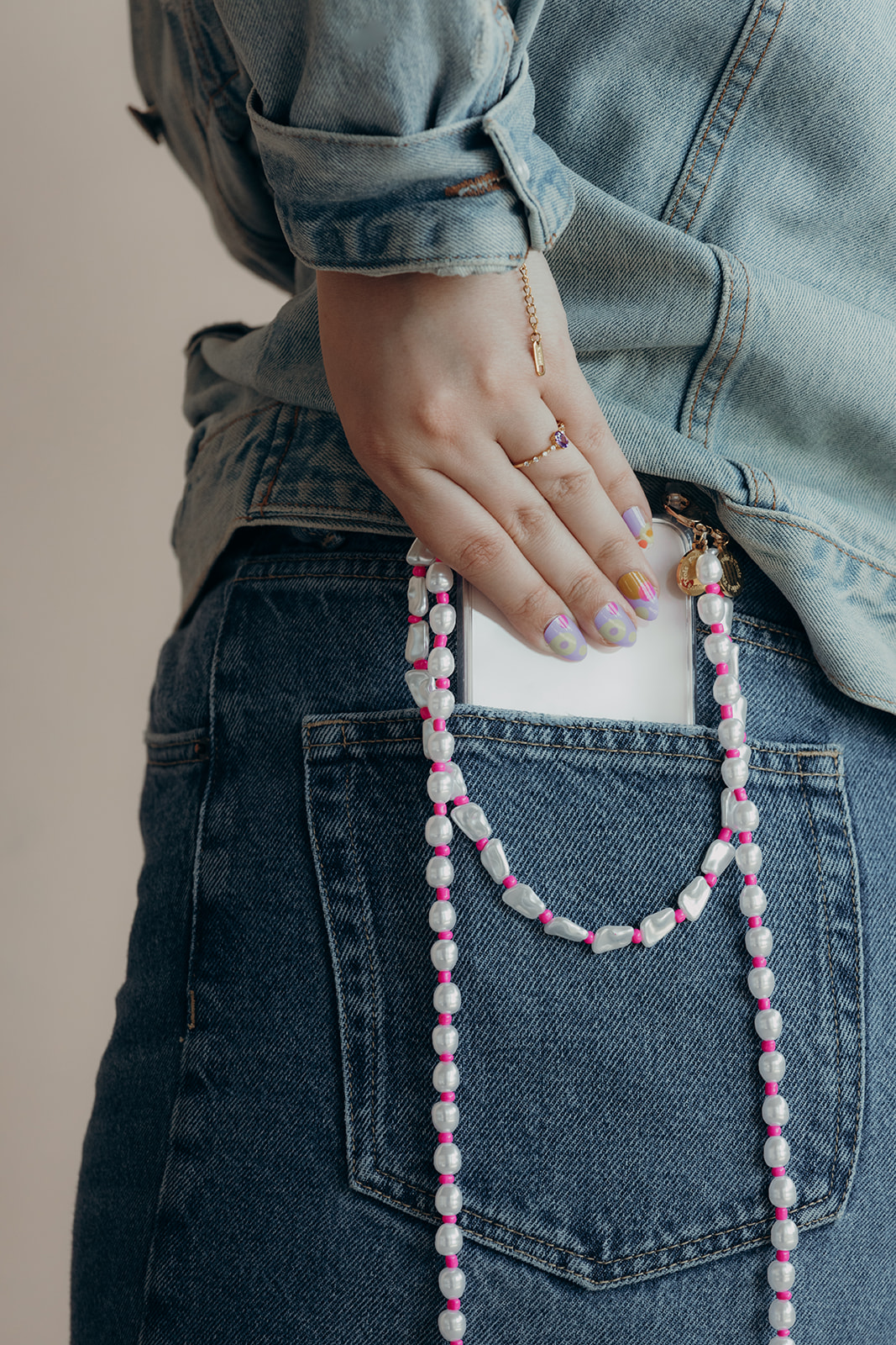White pearl and pink bead Posy Pearl LONG PHONE STRAP looped through a denim jacket pocket holding a phone.