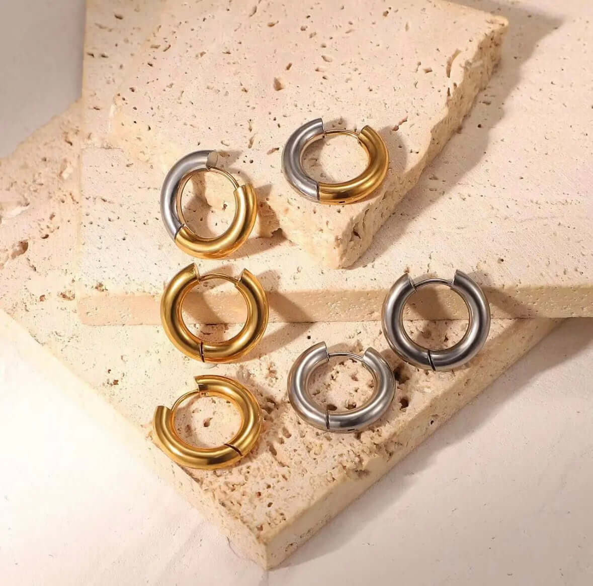 Radiant Bliss Earrings display three pairs of chunky tube hoops in gold and silver, arranged on a stone slab.