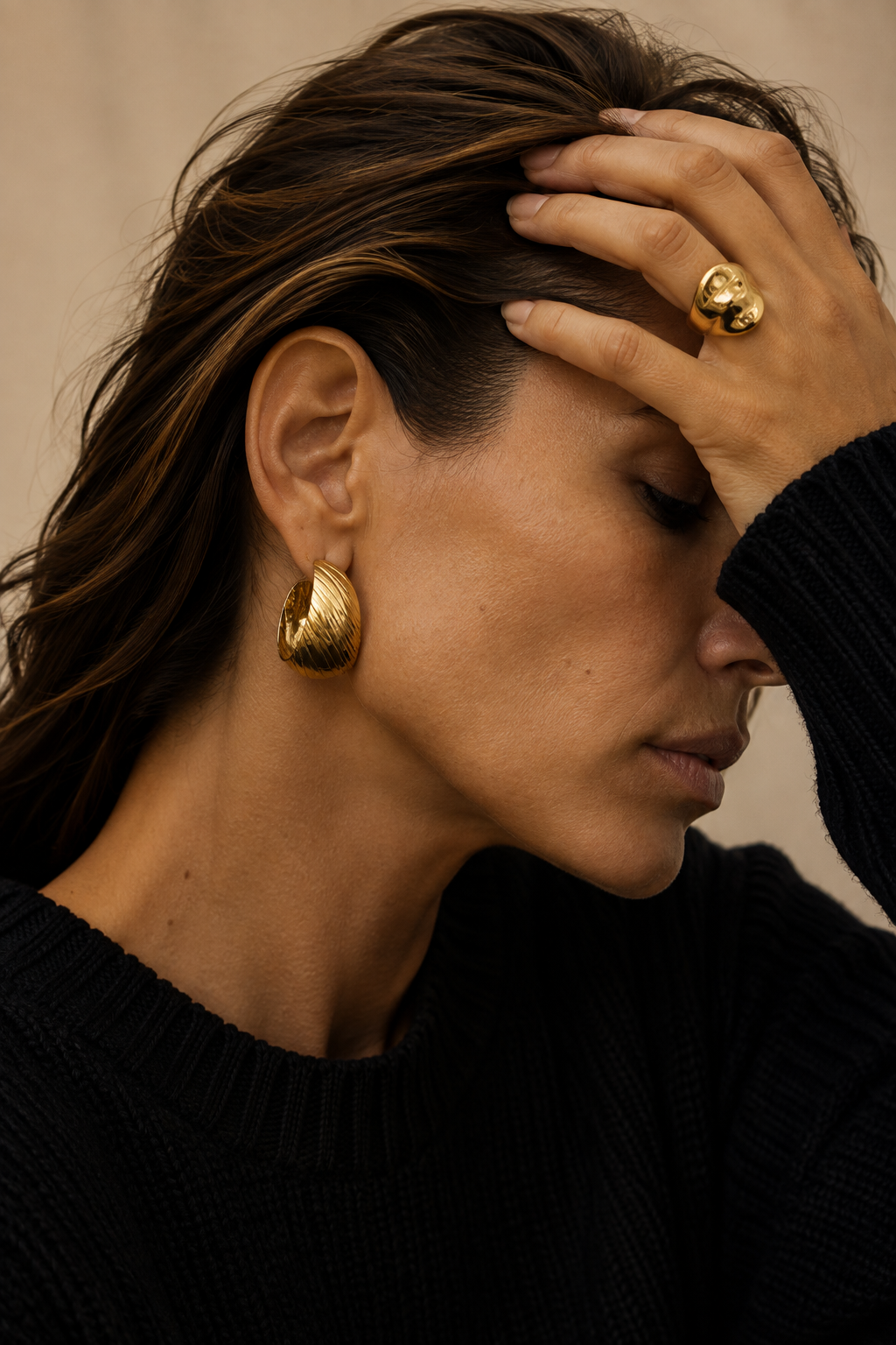 Model with her hand in her hair wears the gold Rally EARRINGS twisted ribbed hoop, styled with a sculptural gold ring.