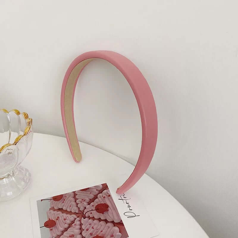 A single dusty rose matte padded headband styled upright near a glass dish and a small photo card.