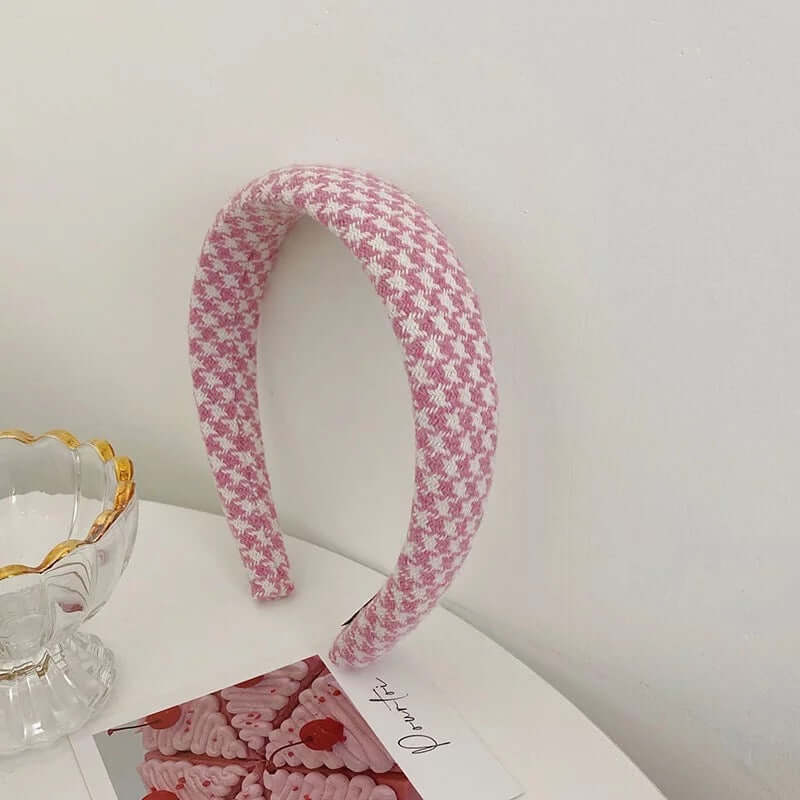 A single pink and white houndstooth check padded headband styled upright near a glass dish and photo card.
