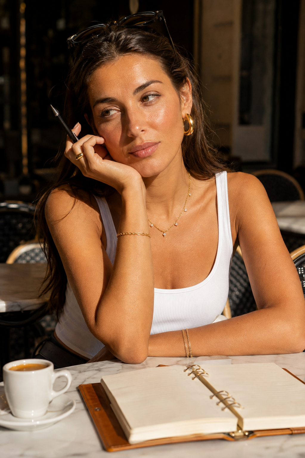 Model at a café table wears the gold Reverie NECKLACE layered with hoop earrings, rings and a fine bracelet.