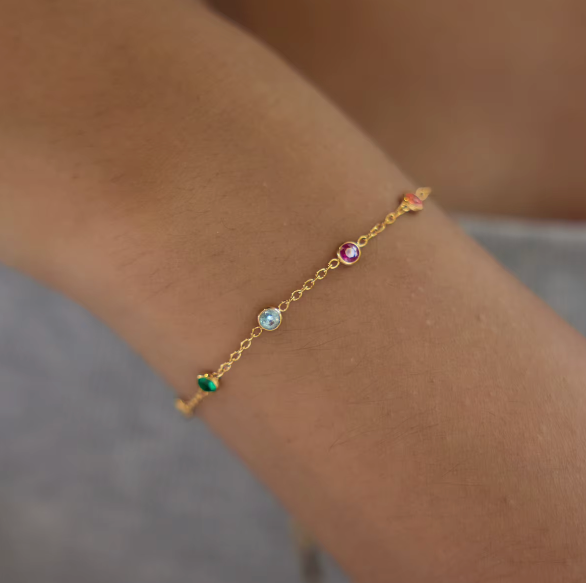 A single gold Riva BRACELET on the wrist, its fine chain dotted with green, aqua, fuchsia and orange bezel-set gemstones.