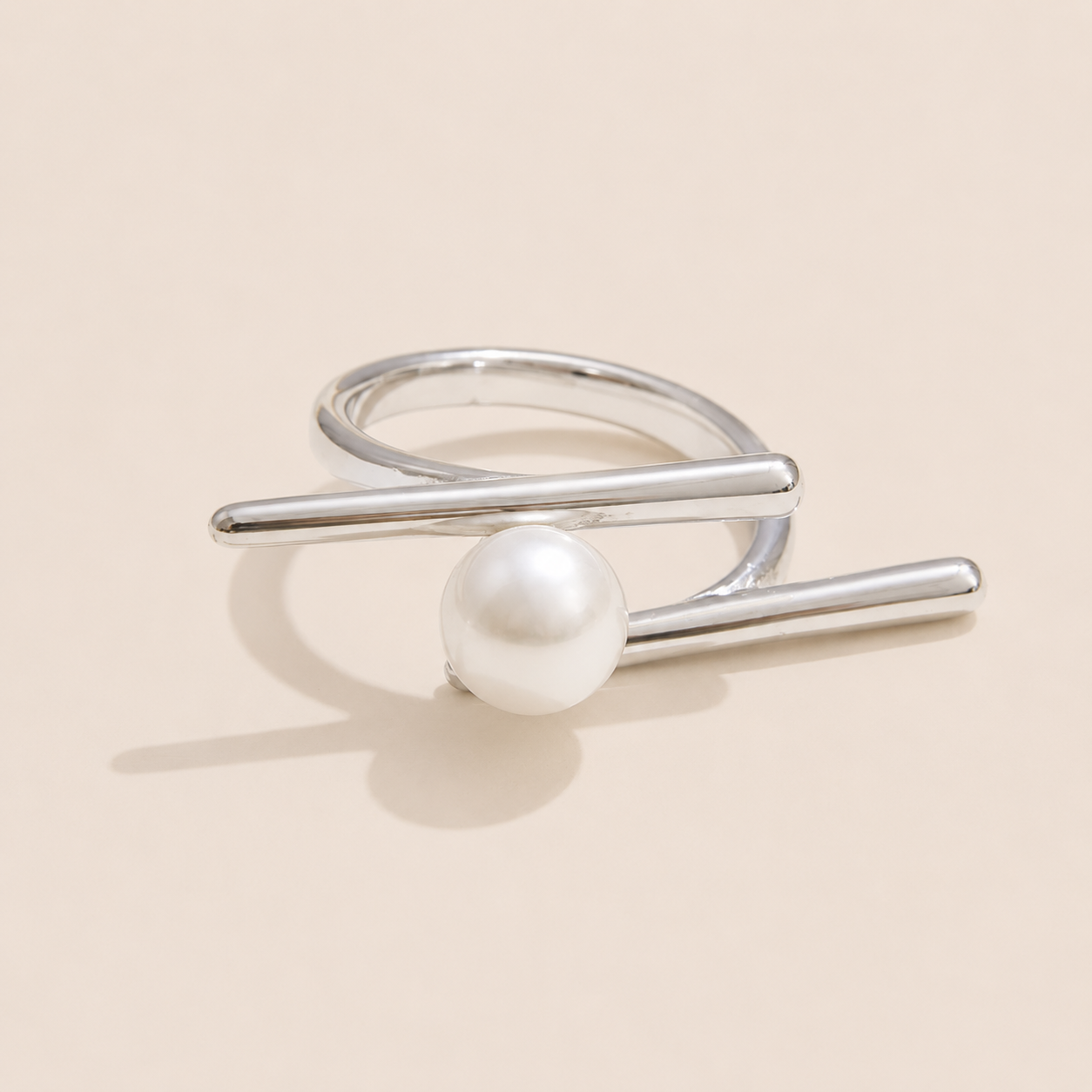 Silver double-band ring with two crossing bars cradling a single round pearl, shown on a cream backdrop — Folie à Trois Riviera Club RING.