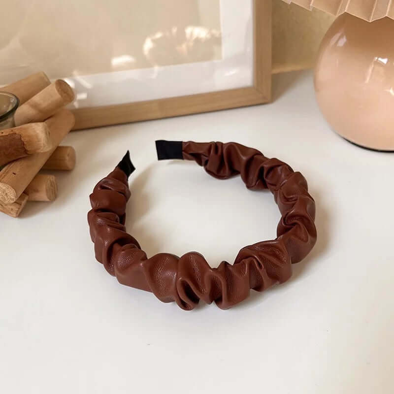 A single dark chestnut brown ruched faux leather Romy HAIRBAND laid flat on a white surface, showing its knotted texture.