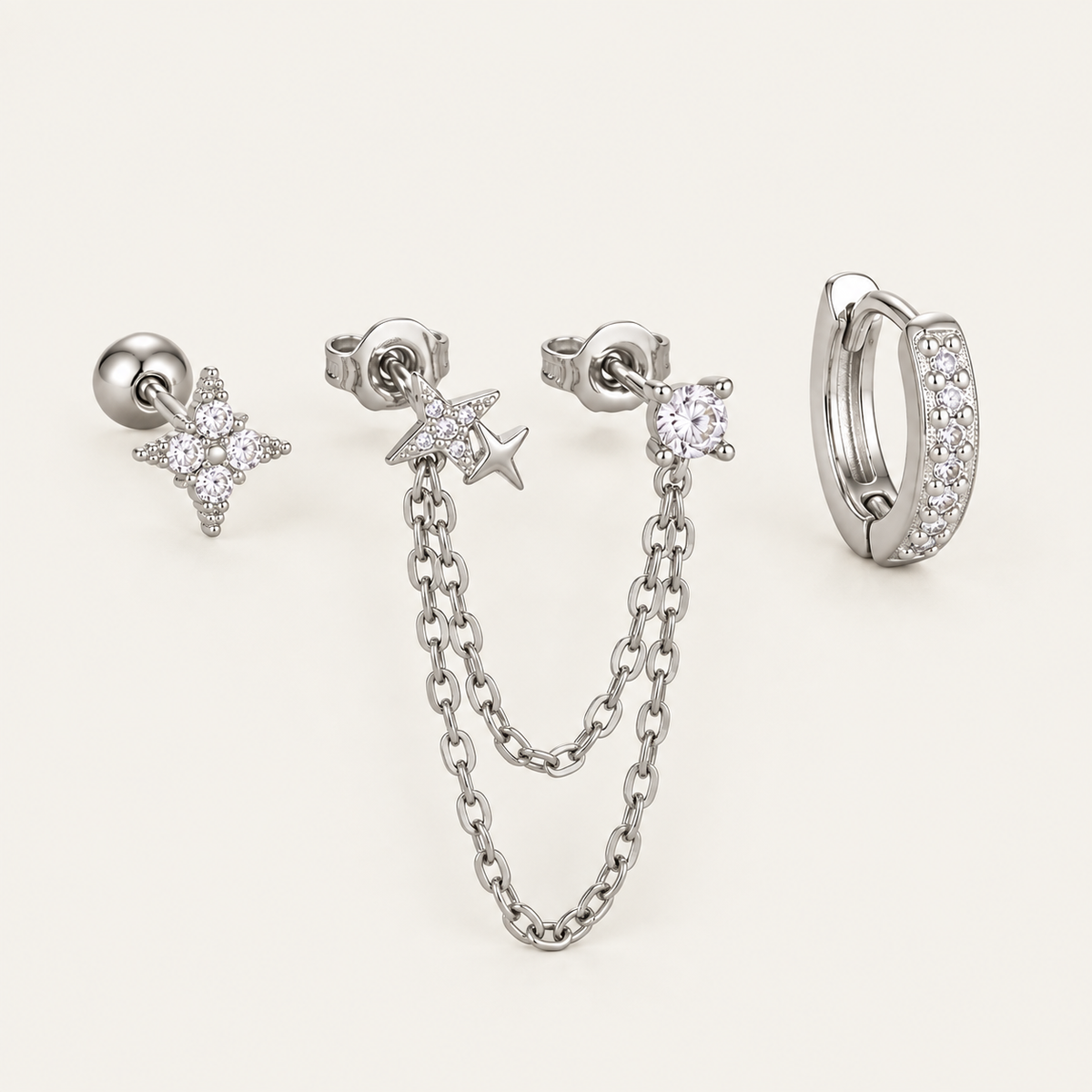 The Folie à Trois Romy SET in silver: a star stud, a star chain-drop earring, a round bezel stud and a pavé huggie hoop.