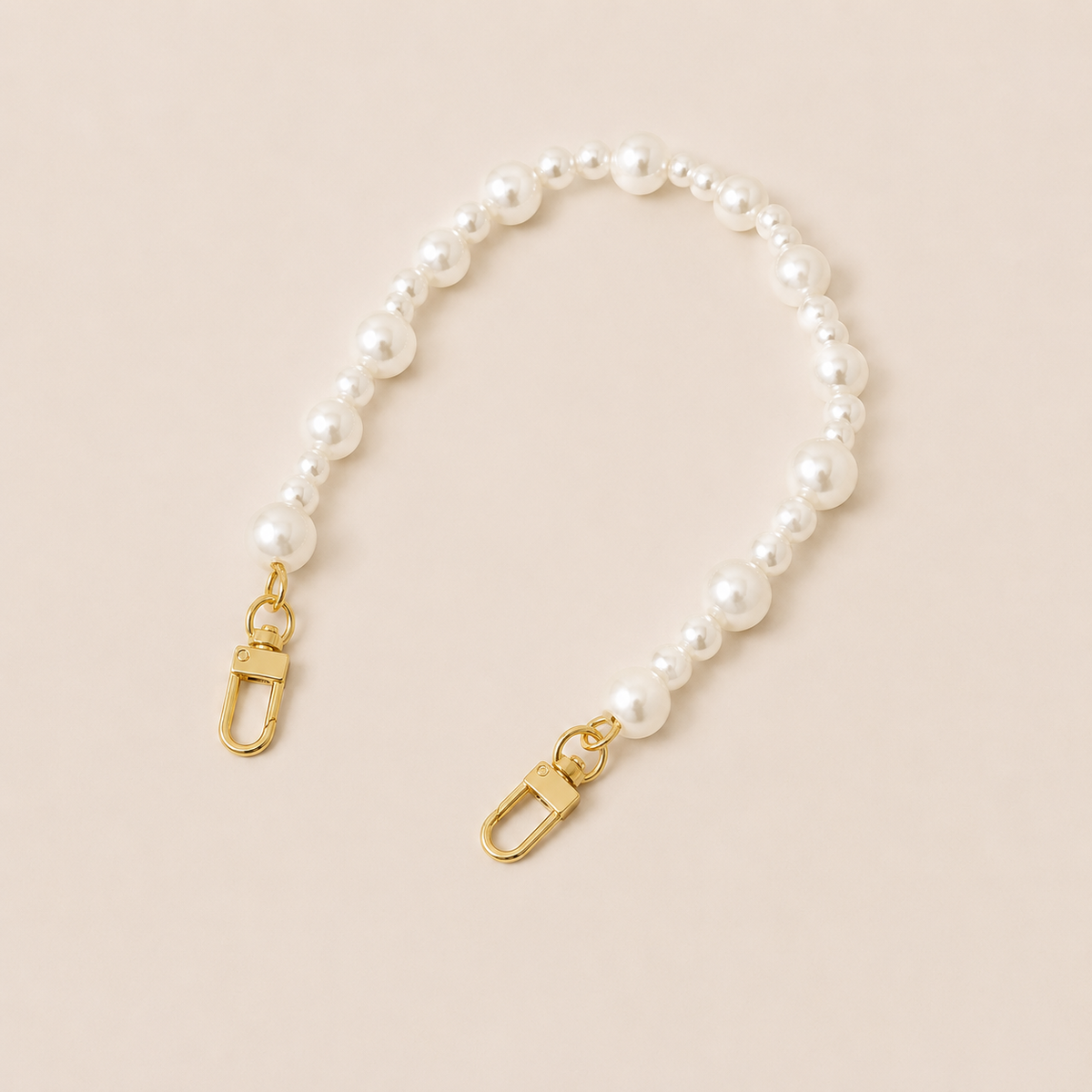 Folie à Trois Sabine Pearl short wholesale phone chain in graduated white pearls with gold clasps, laid flat on a cream background.