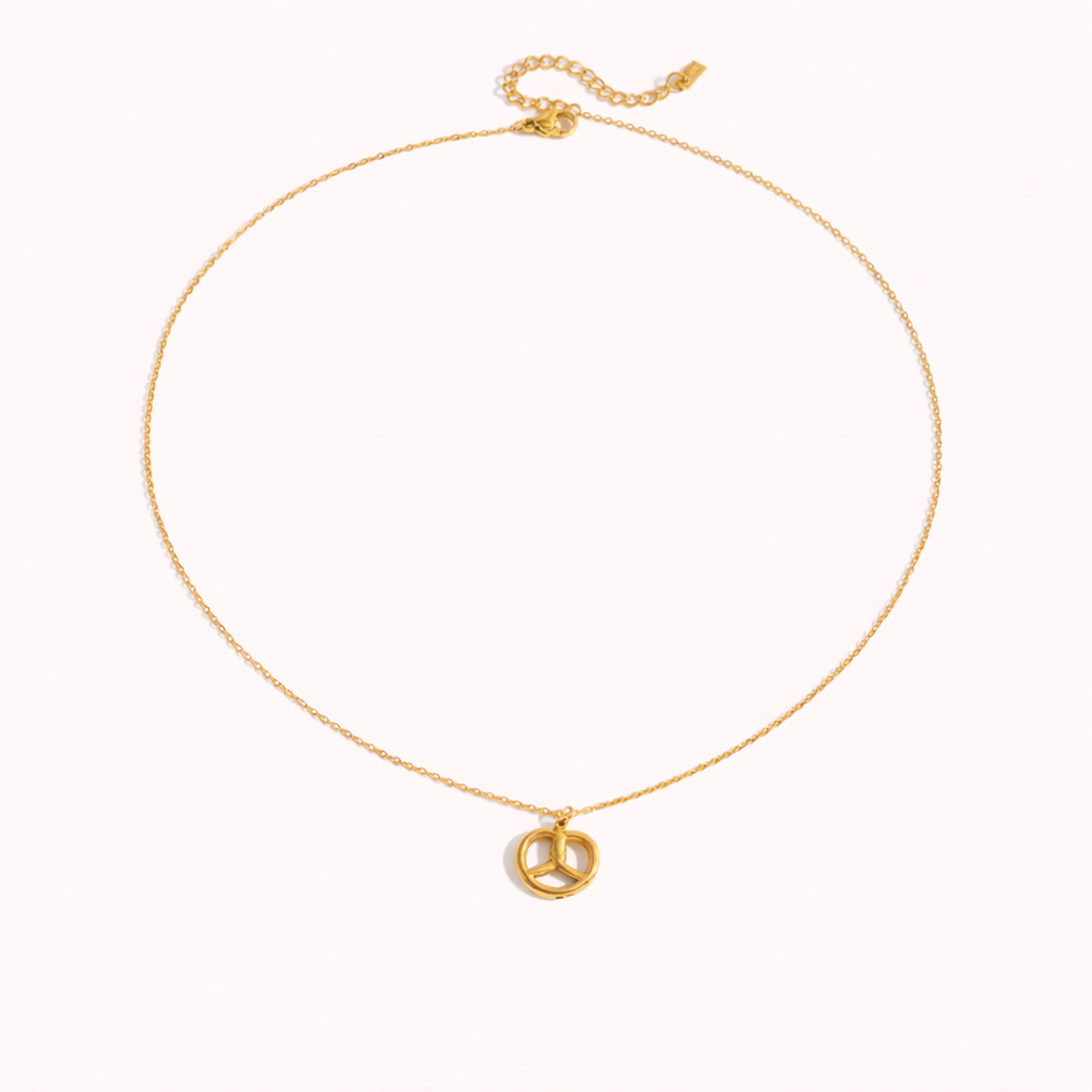 The Salty Sweet NECKLACE laid flat, its gold pretzel-shaped pendant shown alone on a fine chain against a plain background.