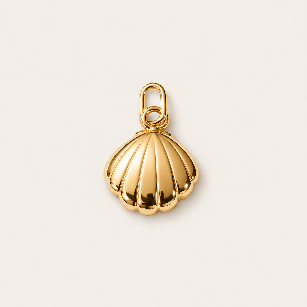 The Shell CHARM in gold, a scalloped clam shell pendant with a ribbed texture, shown in close-up studio photography on cream.
