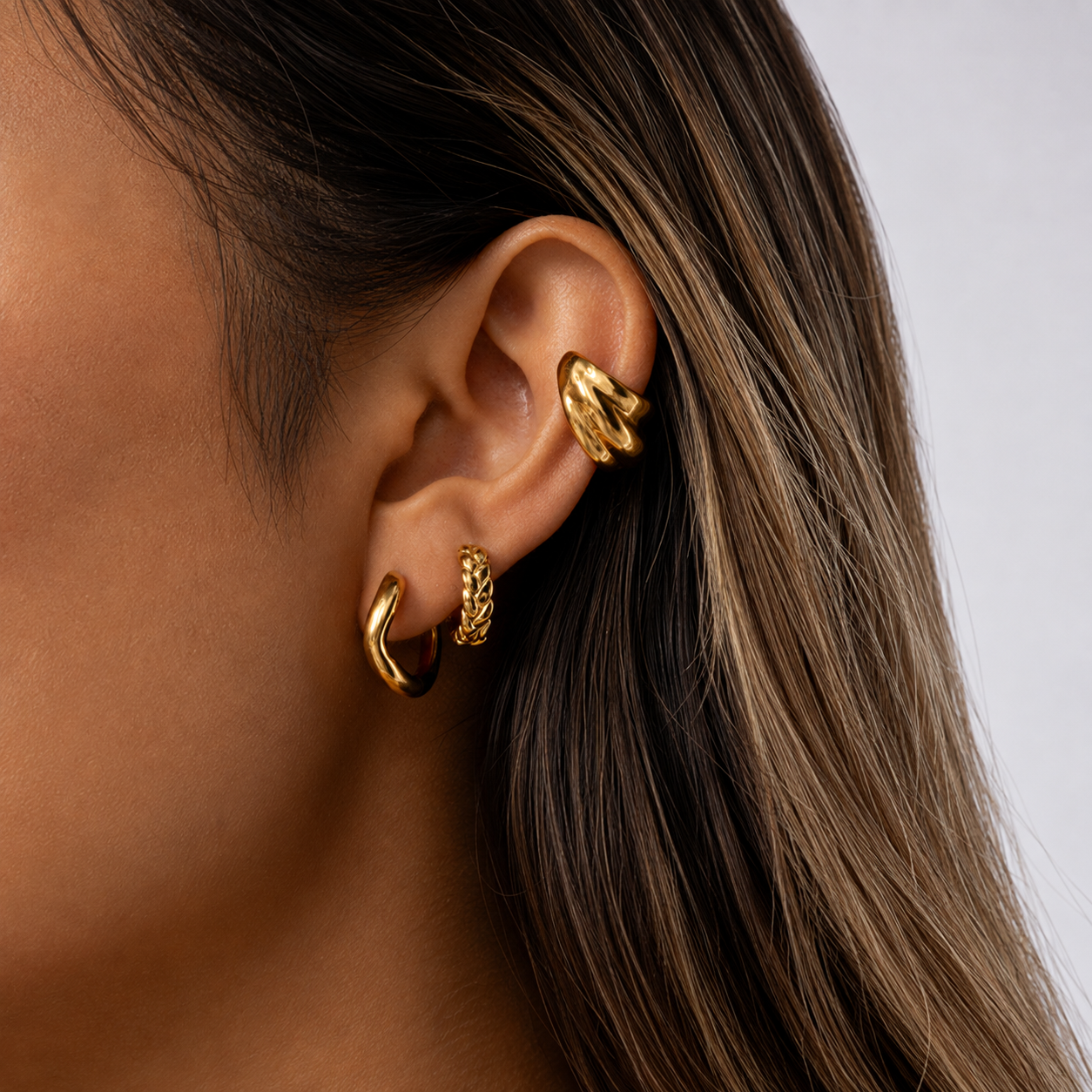 The Shockwave EAR CUFF worn on the ear cartilage, a ribbed gold cuff layered above matching gold hoop earrings.