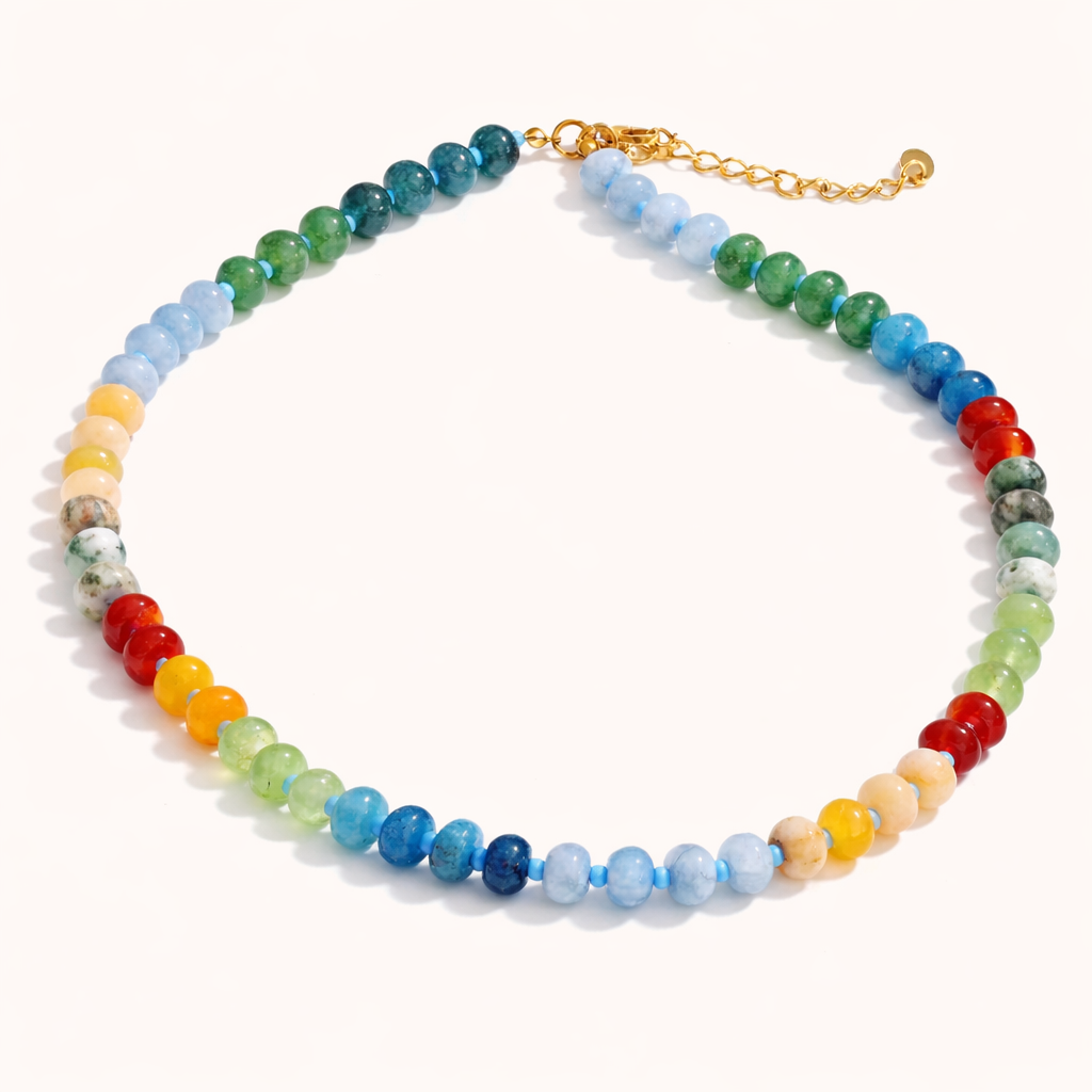 The Sicily NECKLACE laid flat, its multicolor gemstone beads in blue, green, red, and amber shades with a gold extender chain clasp.