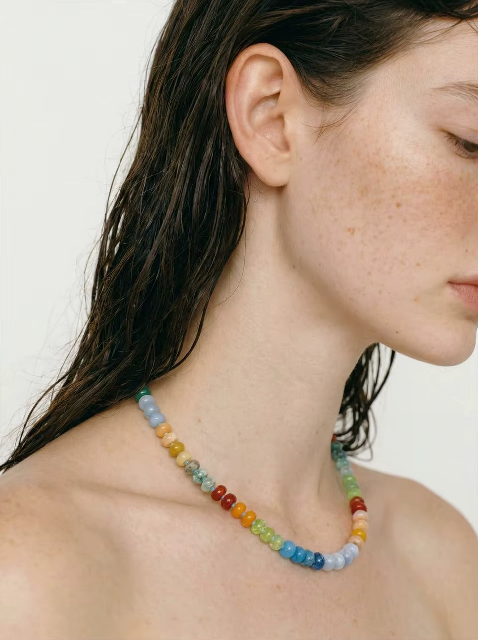 The Sicily NECKLACE worn close-up on bare skin, the model looking down with wet hair against a plain studio background.