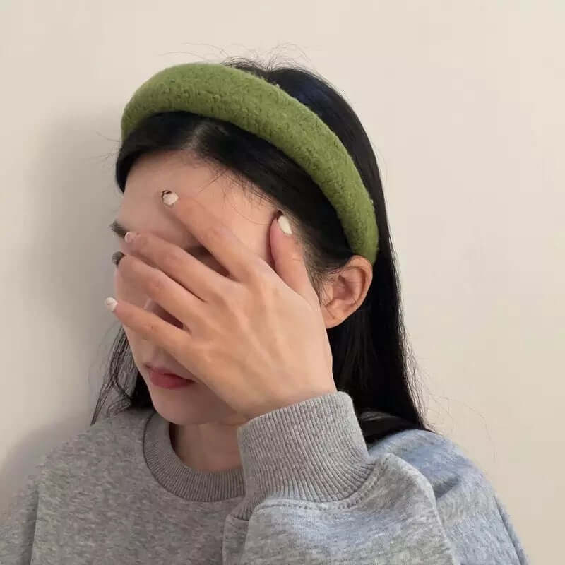 A young woman wearing an olive green boucle padded Skylar HAIRBAND, with her hand raised covering her eyes.