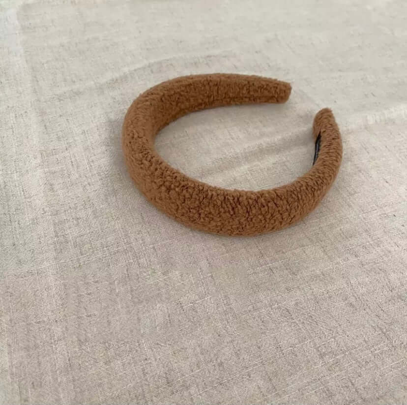 A single camel tan boucle padded Skylar HAIRBAND laid on linen fabric.