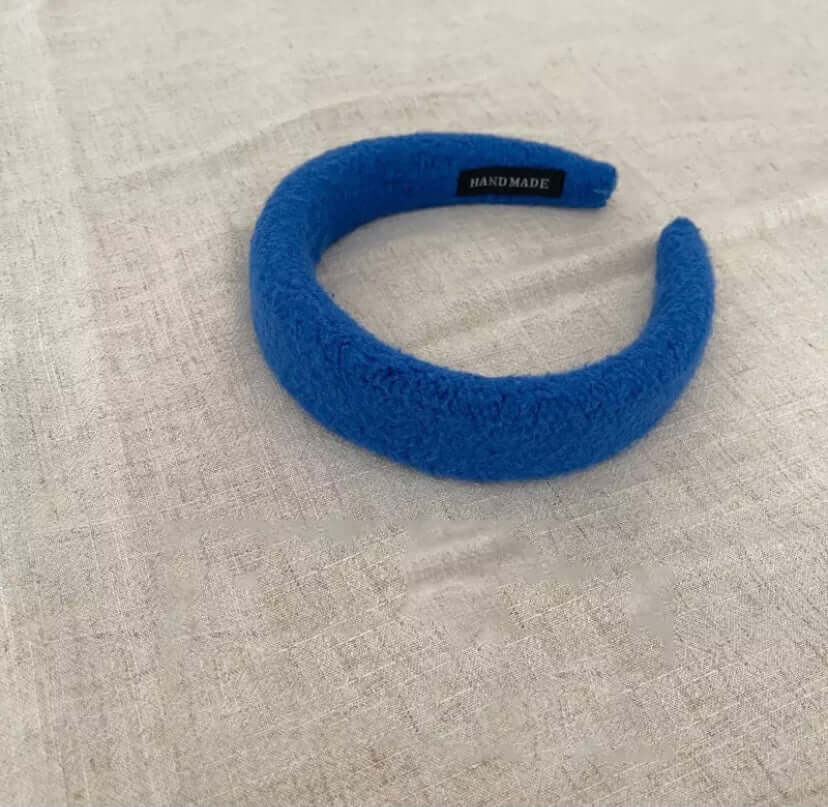 A single cobalt blue boucle padded Skylar HAIRBAND with a handmade label tag, laid on linen fabric.