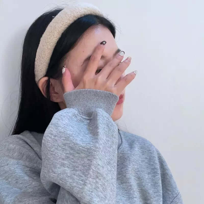 A young woman wearing a cream boucle padded Skylar HAIRBAND, with her hand raised covering her face.