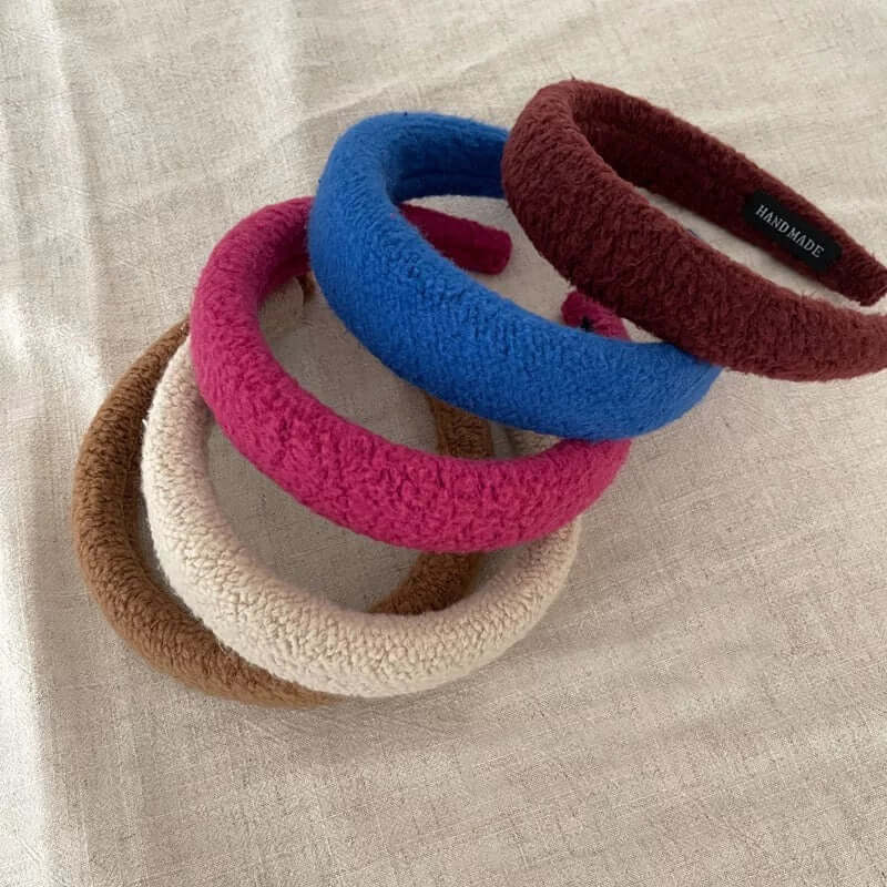A group of four Skylar HAIRBAND boucle padded headbands in blue, magenta, cream and burgundy stacked together on linen.