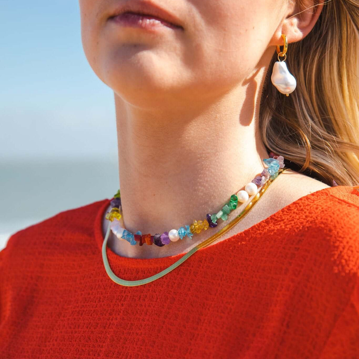 The Snake Skin NECKLACE in gold layered with a multicolor beaded gemstone necklace, worn at the neckline in beach sunlight.