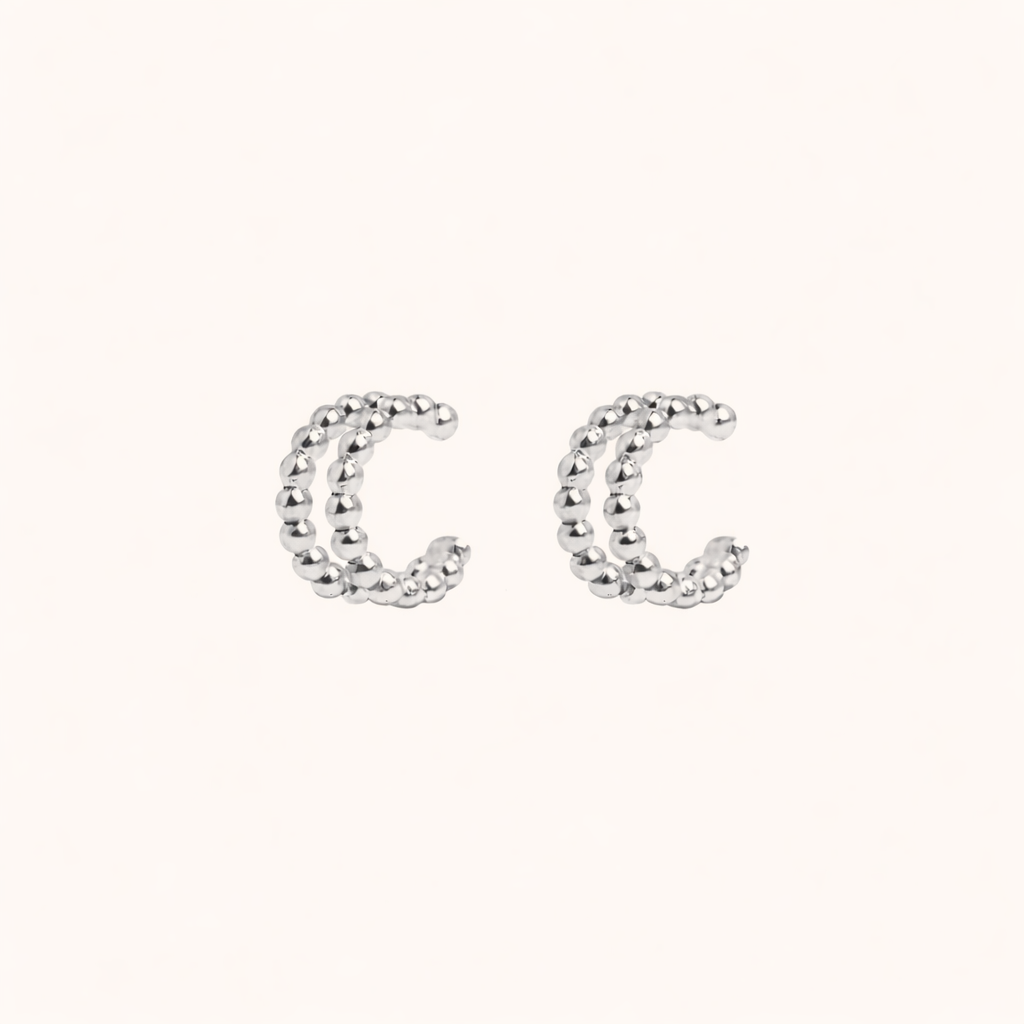 The Solara EAR CUFF in silver, a pair of double-band beaded cuffs shown side by side on a cream background.