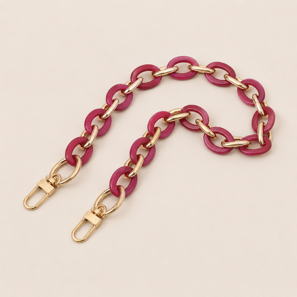Folie à Trois Sorrel wholesale phone chain in fuchsia acetate rings with gold links and gold clasps, laid flat on a cream background.